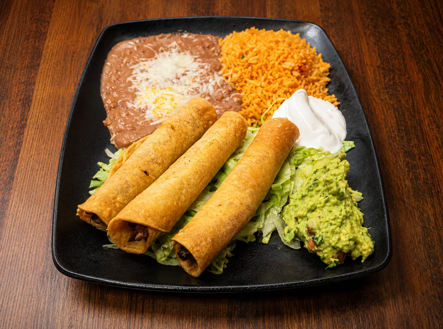 Three taquitos with guacamole, sour cream, rice and beans